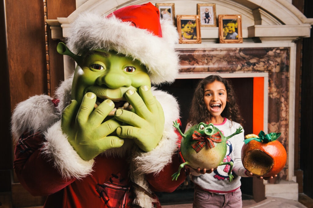 Shrek the ogre wearing a Santa hat with a happy child, celebrating Christmas in London.