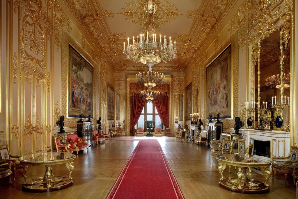 An opulent golden room in Windsor Castle full of priceless decorations and a red carpet.