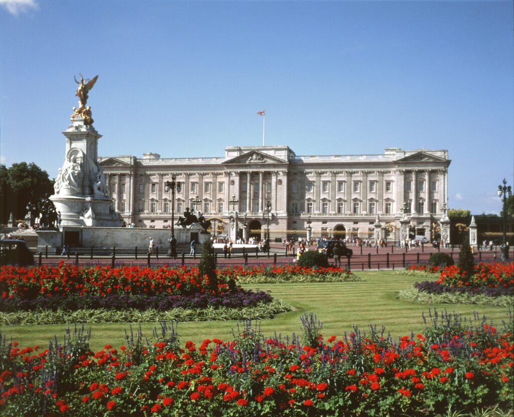 An exterior view of Buckingham Palace, featuring colourful flowers in the foreground.