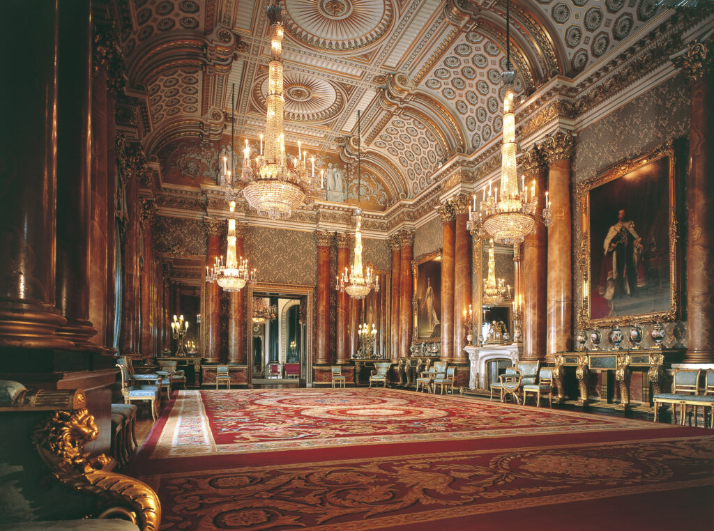 The inside of the Blue Drawing Room at Buckingham Palace, featuring opulent red and gold decorations as well as blue furniture.