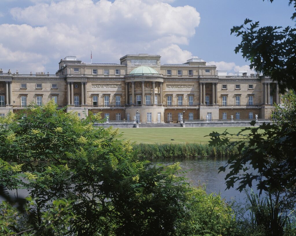 A view of Buckingham Palace from the back, with grass and water in the foreground.
